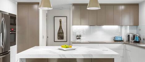 A modern kitchen with a central island, pendant lighting, and stainless steel appliances.