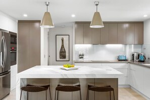 A modern kitchen with a central island, pendant lighting, and stainless steel appliances.