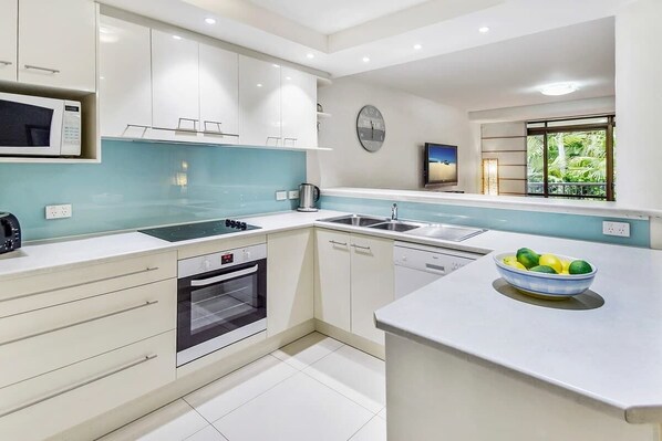 A modern kitchen with white cabinets, a microwave, an oven, a sink, and a window with a view of greenery.
