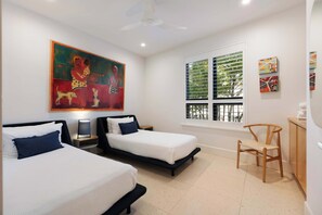 A hotel room with two beds, a desk, a chair, a painting, and a window with blinds.