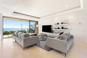 A modern living room with a large TV, comfortable seating, and a view of the ocean.