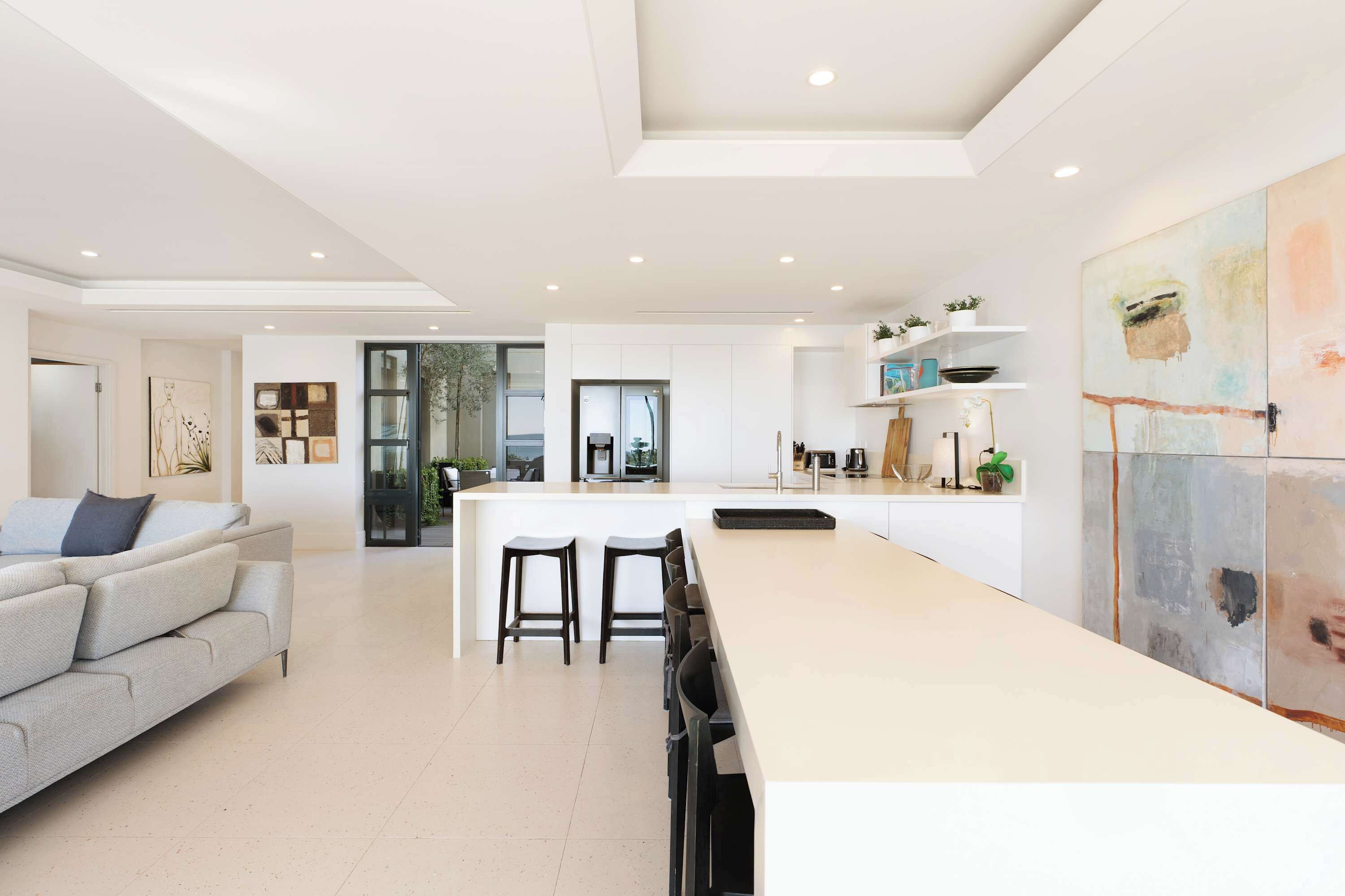 A modern kitchen with a central island, bar stools, and a dining area with a sofa.