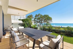 An outdoor patio with a table and chairs, overlooking a beach and ocean.
