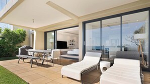 A modern outdoor living area with a patio, lounge chairs, a table, and a grill.