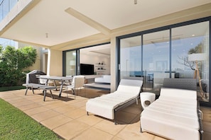 A modern outdoor living area with a patio, lounge chairs, a table, and a grill.
