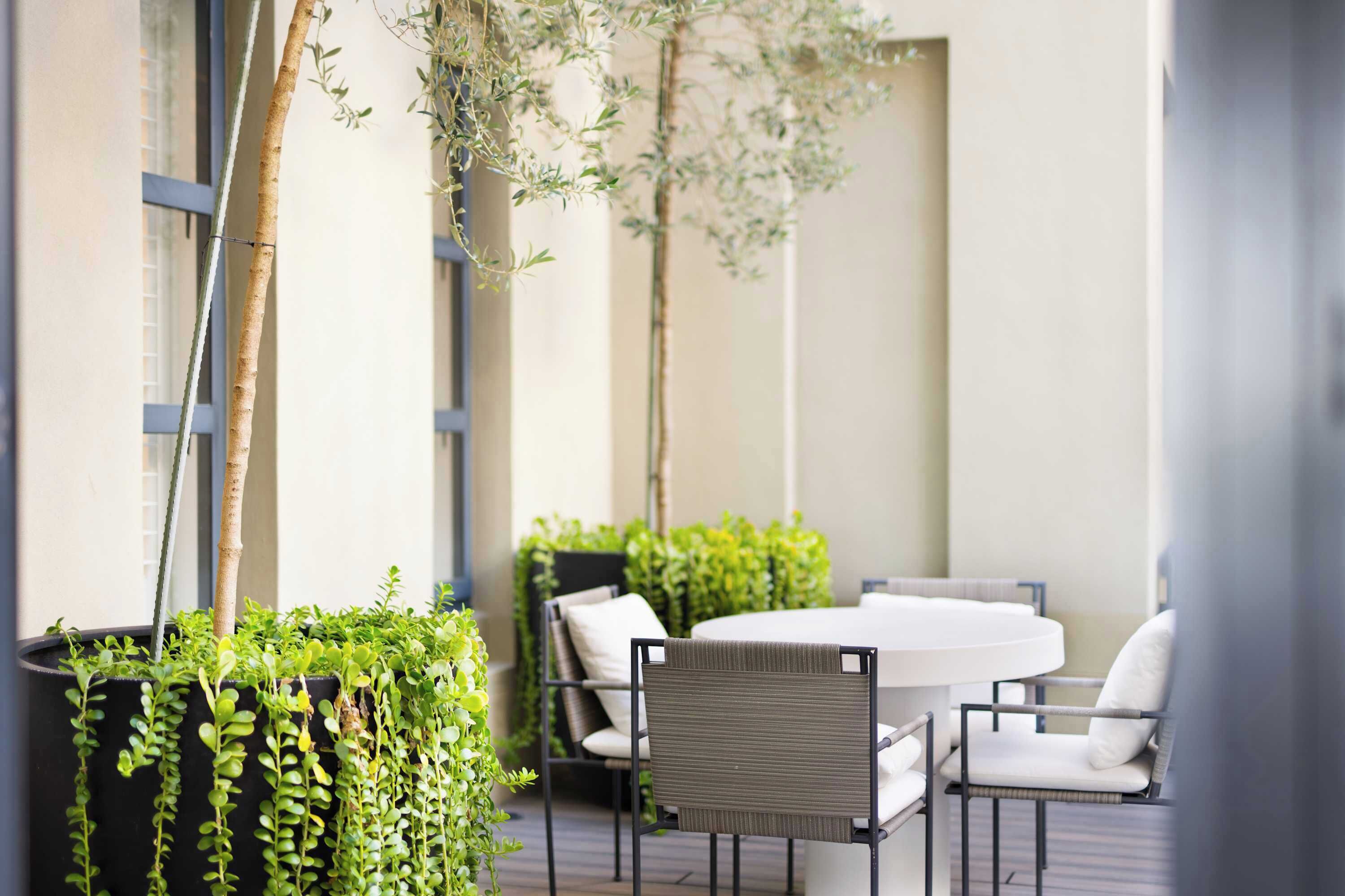 An outdoor seating area with a round table and chairs, surrounded by potted plants and a vertical garden.