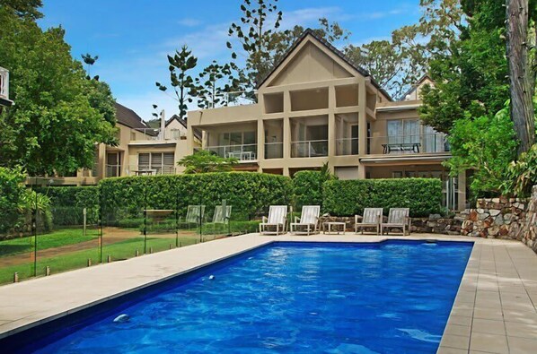 A swimming pool with lounge chairs, a house with a balcony, and a well-maintained lawn.