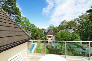 Varanda com guarda-corpo de vidro com vista para uma área residencial, uma cadeira branca e céu claro.