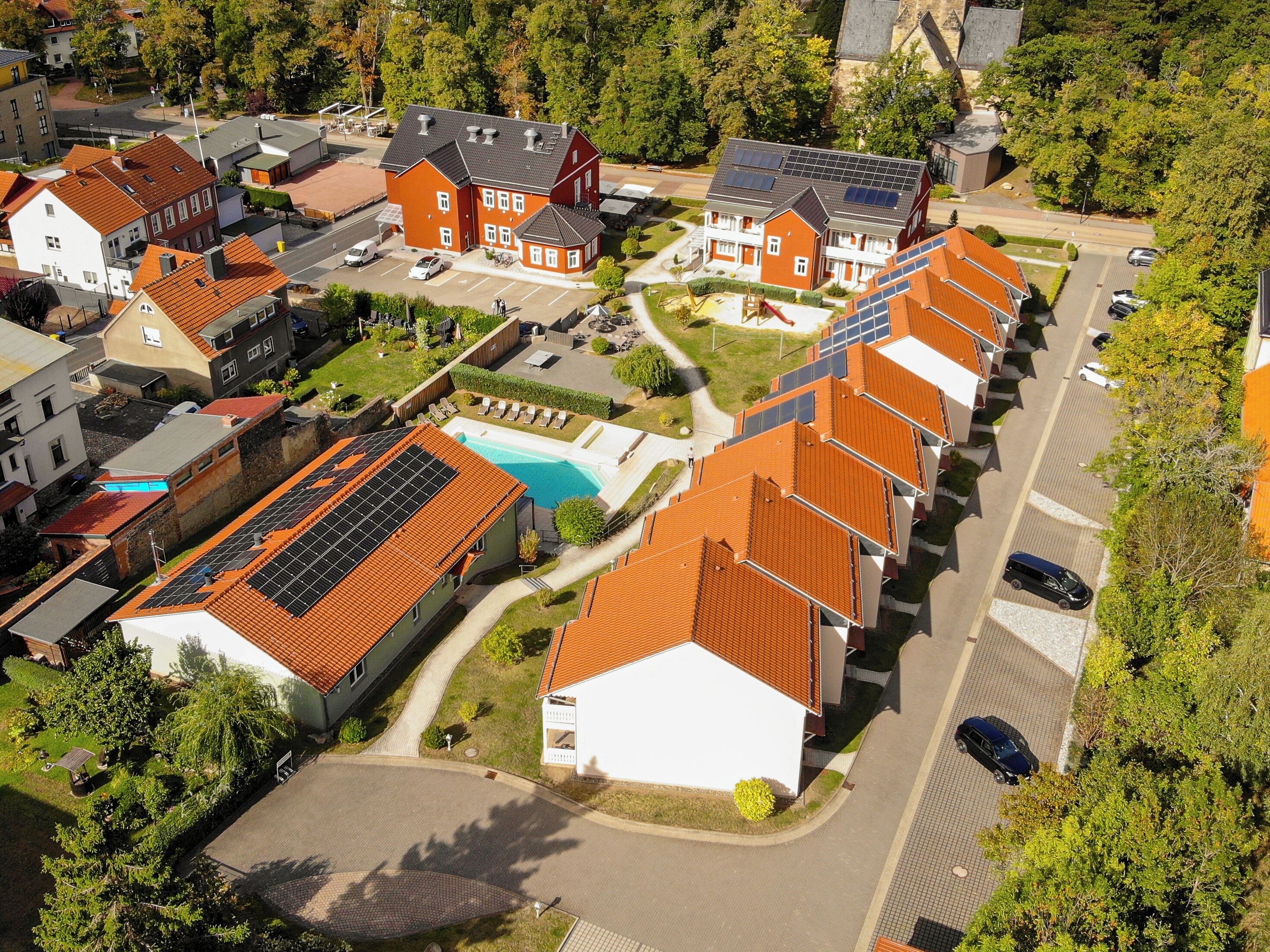 Eine Luftaufnahme einer Wohngegend mit Häusern, die rote Ziegeldächer, Solaranlagen und einen Swimmingpool haben.