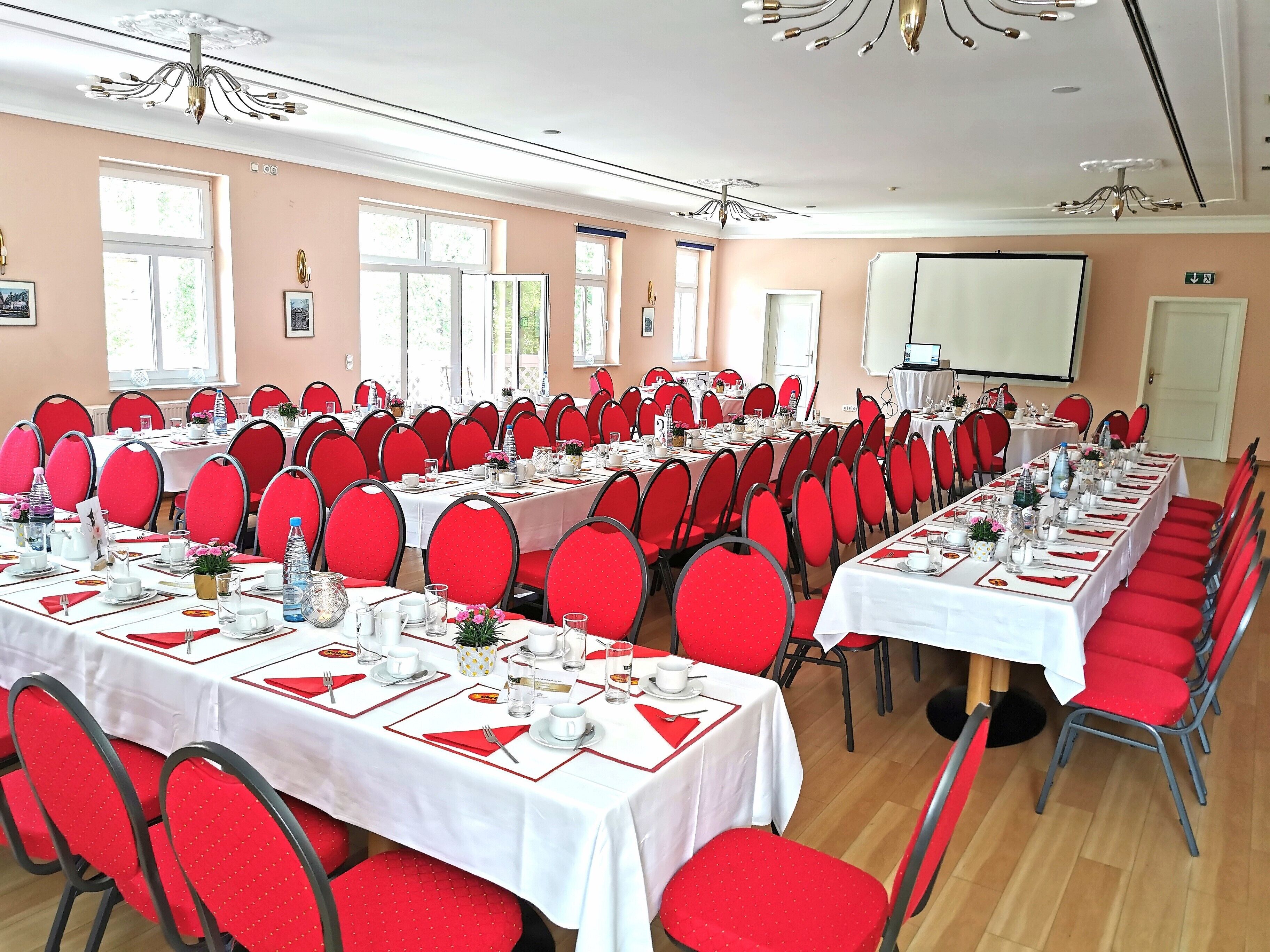 A conference room with multiple tables set for a meeting, red chairs, and a projector screen.