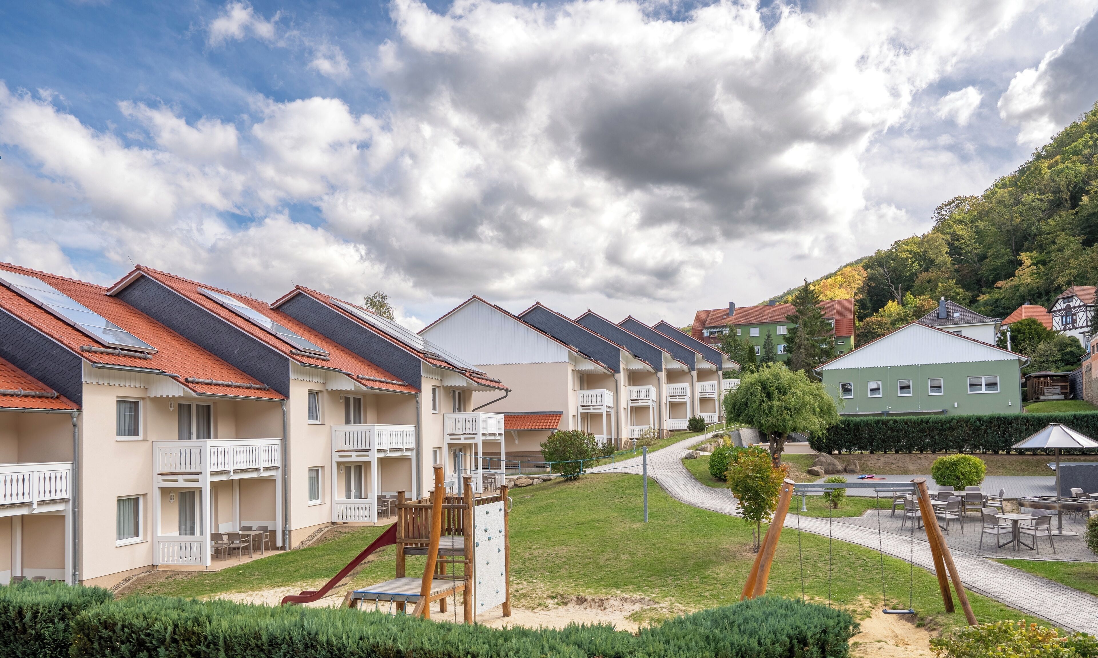 Una hilera de edificios de apartamentos modernos con tejados de tejas rojas, balcones y un área de juegos.