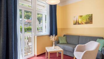 A living room with a sofa, a chair, a table with a vase, and a painting on the wall.