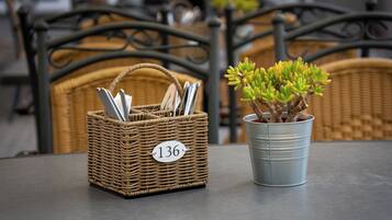 Una cesta de mimbre con la etiqueta '136', cubiertos y una planta en maceta sobre una mesa.