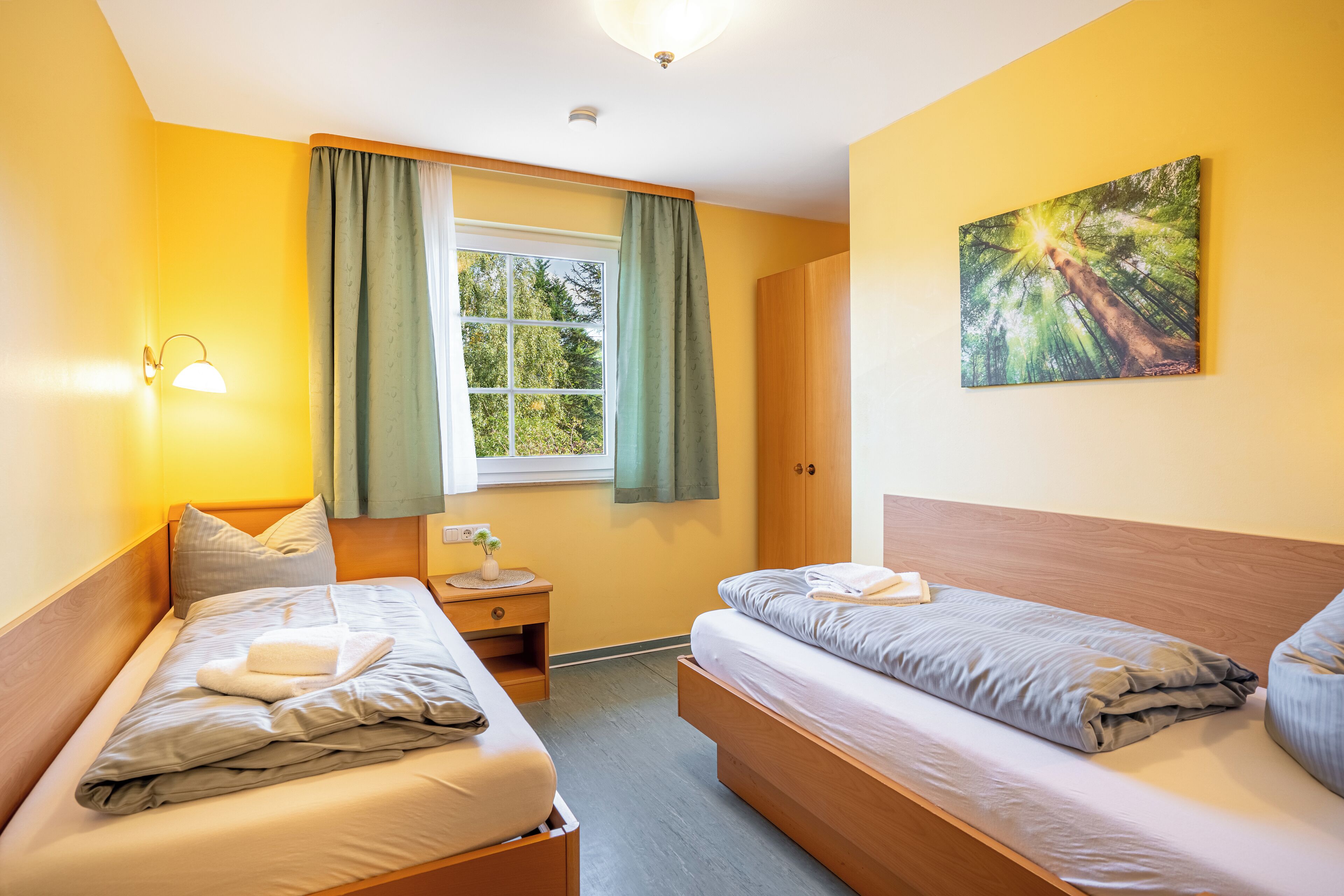 Une chambre avec deux lits, une fenêtre avec des rideaux, un tableau accroché au mur et une table de chevet avec une lampe.