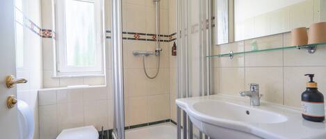 A bathroom with a shower, toilet, sink, and a window.