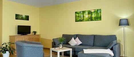 Una sala de estar con un sofá, dos sillones, una mesa de centro, un televisor y una lámpara de pie.