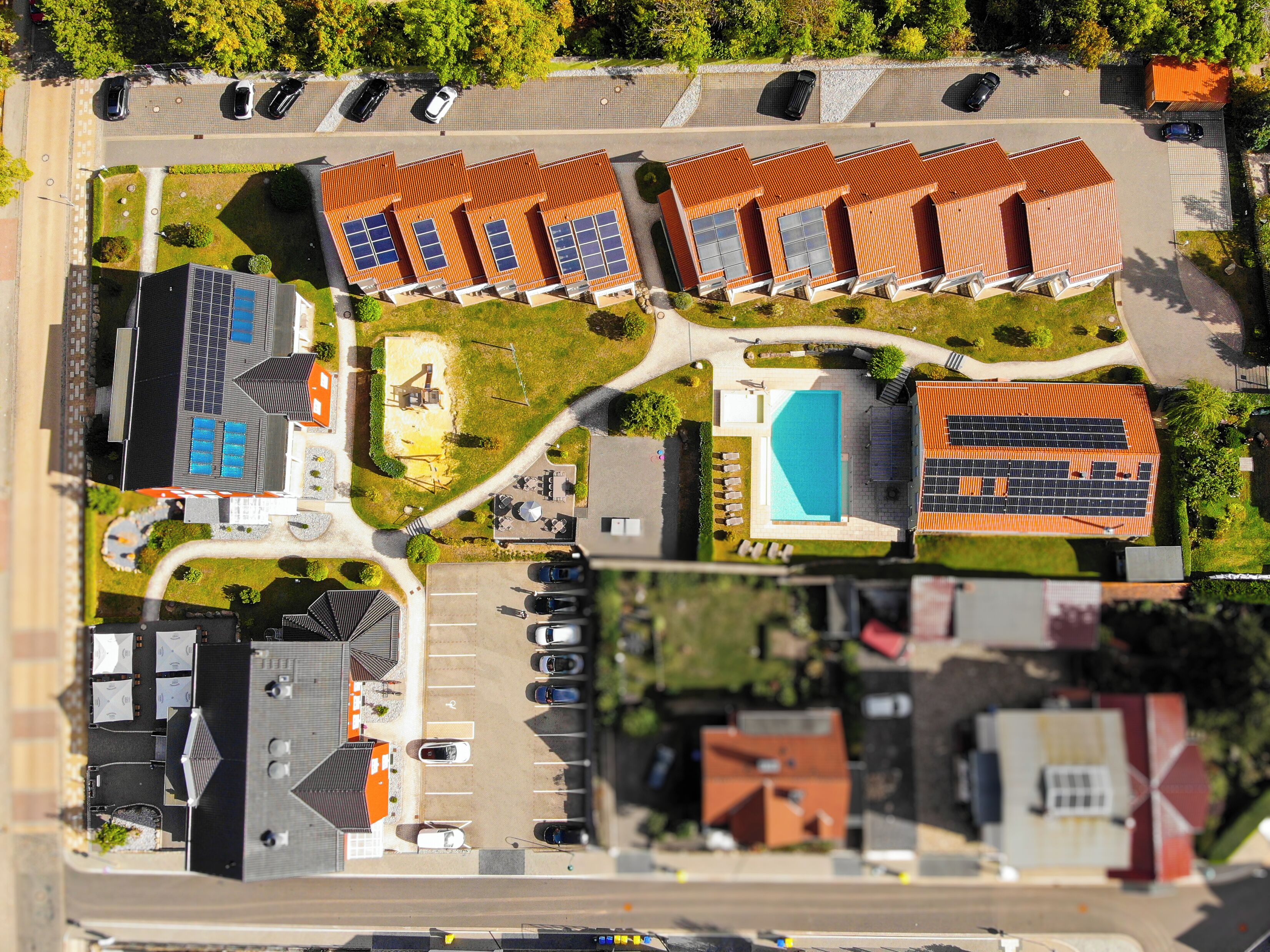 An aerial view of a residential area with multiple houses, a swimming pool, and a parking lot.