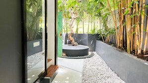 Un jardin intérieur moderne, avec un arbre central, entouré de galets blancs et de plantes de bambou.