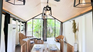 Un coin repas avec une table dressée pour deux personnes, entouré de chaises en osier, sous un ventilateur de plafond dont les ampoules sont apparentes.