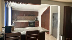 A kitchen with dark wooden cabinets, a granite countertop, a built-in oven, a microwave, and a stainless steel refrigerator. - Home in Flamingos Residencial. (Bucerías)