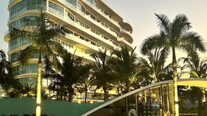 A multi-story hotel with a curved facade, palm trees, and a glass entrance. - Home in Flamingos Residencial. (Bucerías)