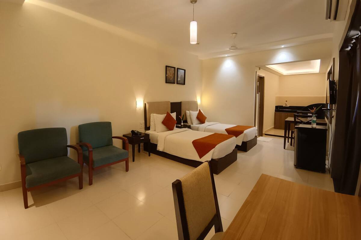 A hotel room with two single beds, a desk, a chair, and a dining table.