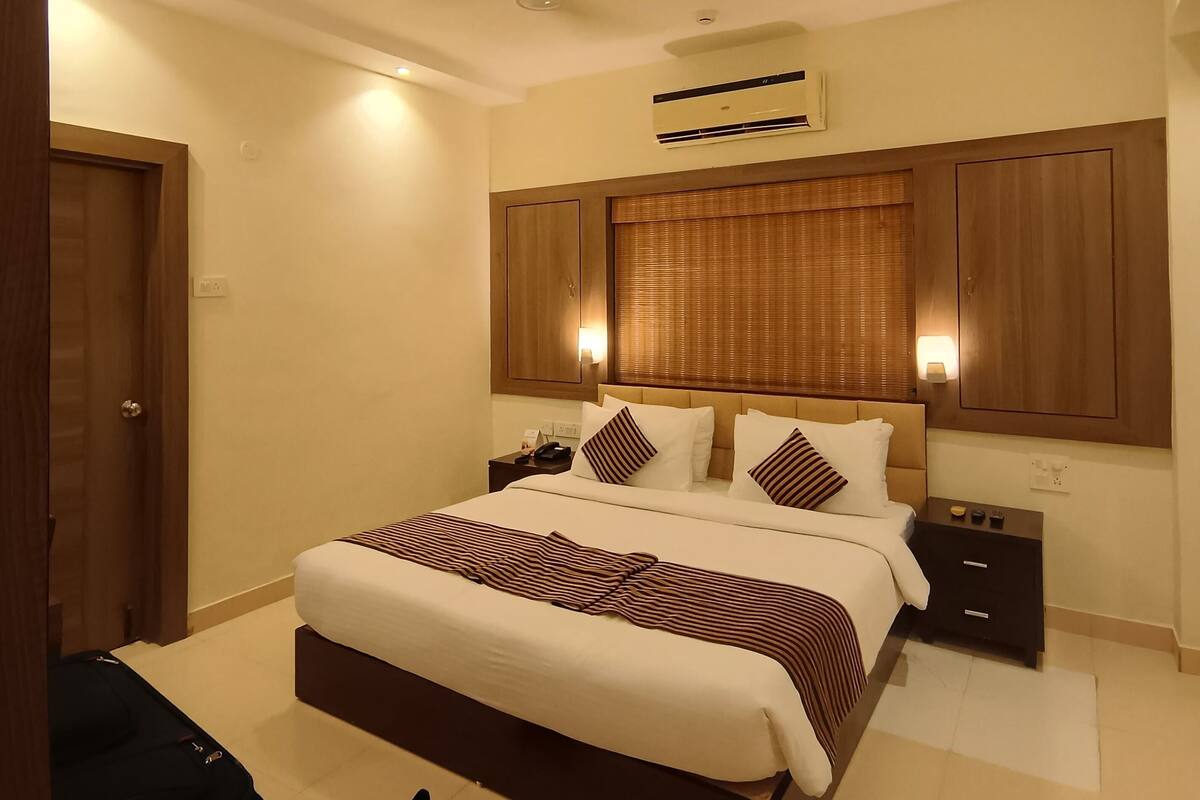 A hotel room with a large bed, a bedside table, a wardrobe, and an air conditioning unit.