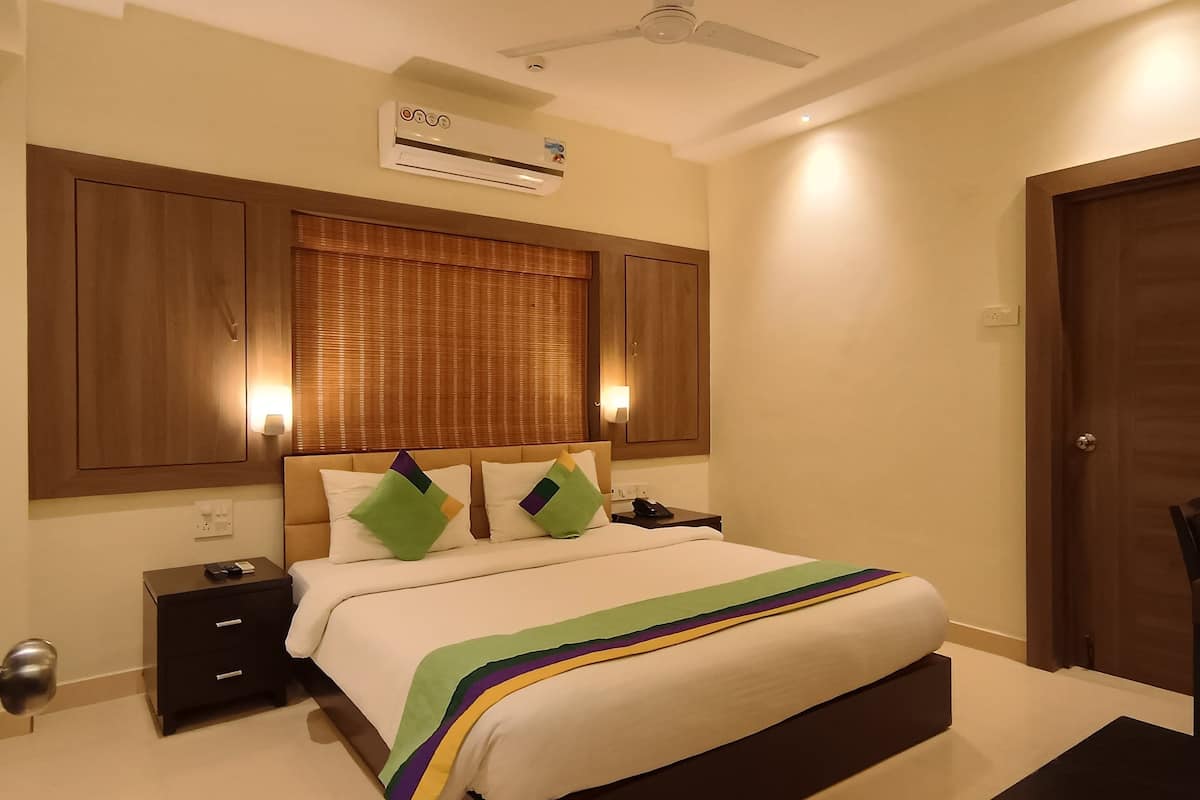A hotel room with a bed, bedside tables, a ceiling fan, an air conditioning unit, and a door.