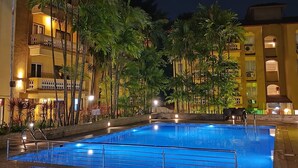 Ein Pool mit gewölbter Kante, umgeben von Palmen und einem Gebäude mit Balkonen.