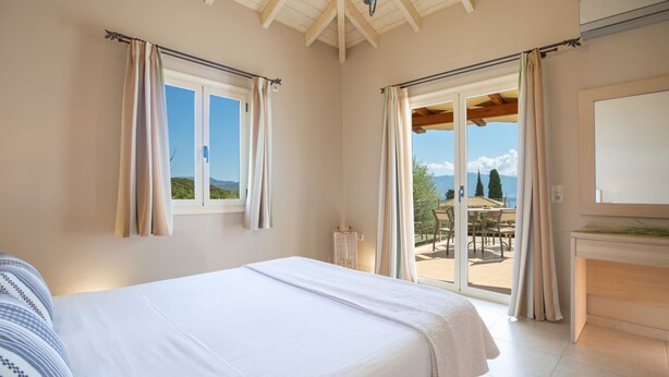 Ein Schlafzimmer mit einem großen Bett, Blick ins Freie und einer Schiebetür zu einer Terrasse.