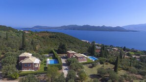 Ein Küstenanwesen mit mehreren Häusern, einem Pool und Blick auf Meer und Berge.