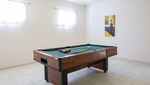 Ein Billardtisch in einem Raum mit weißen Wänden, zwei mit Vorhängen versehenen Fenstern und einem Gemälde an der Wand.