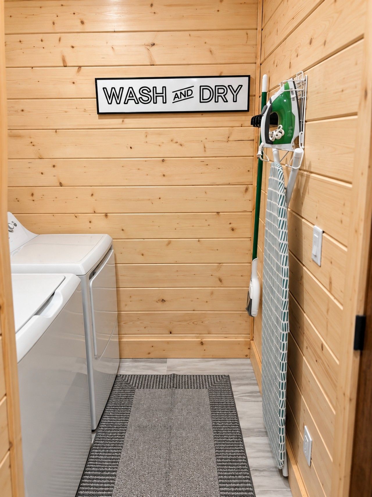 A compact wash and dry room with wooden walls, a washing machine, a drying rack, and a sign indicating the room's purpose.
