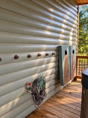 Eine Holzterrasse mit einem an der Wand liegenden Schlauch, einem Metallgeländer und einer Holztür.