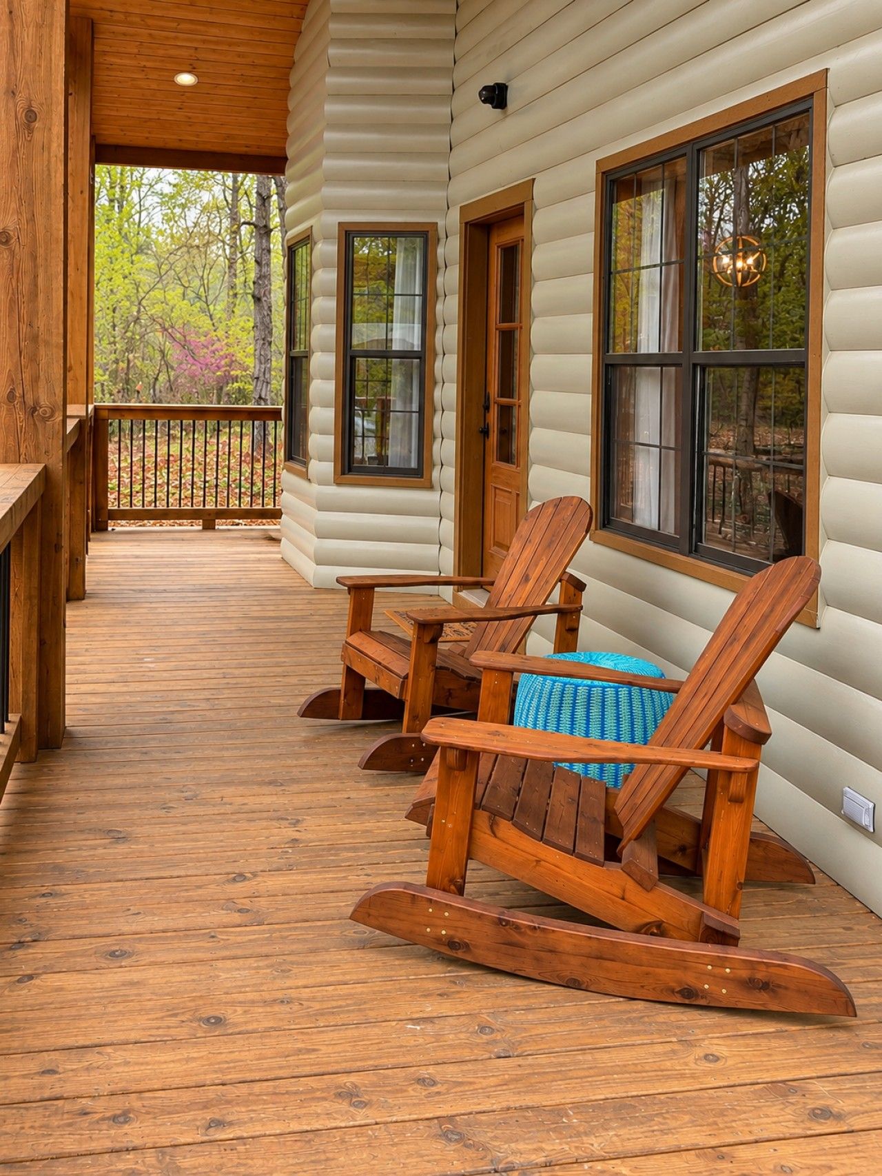 A log cabin with a wooden deck, rocking chairs, and a view of the forest.