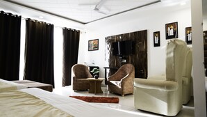 Habitació d'hotel moderna amb un llit gran, dos seients còmodes, una taula rodona petita i un televisor penjat a la paret.