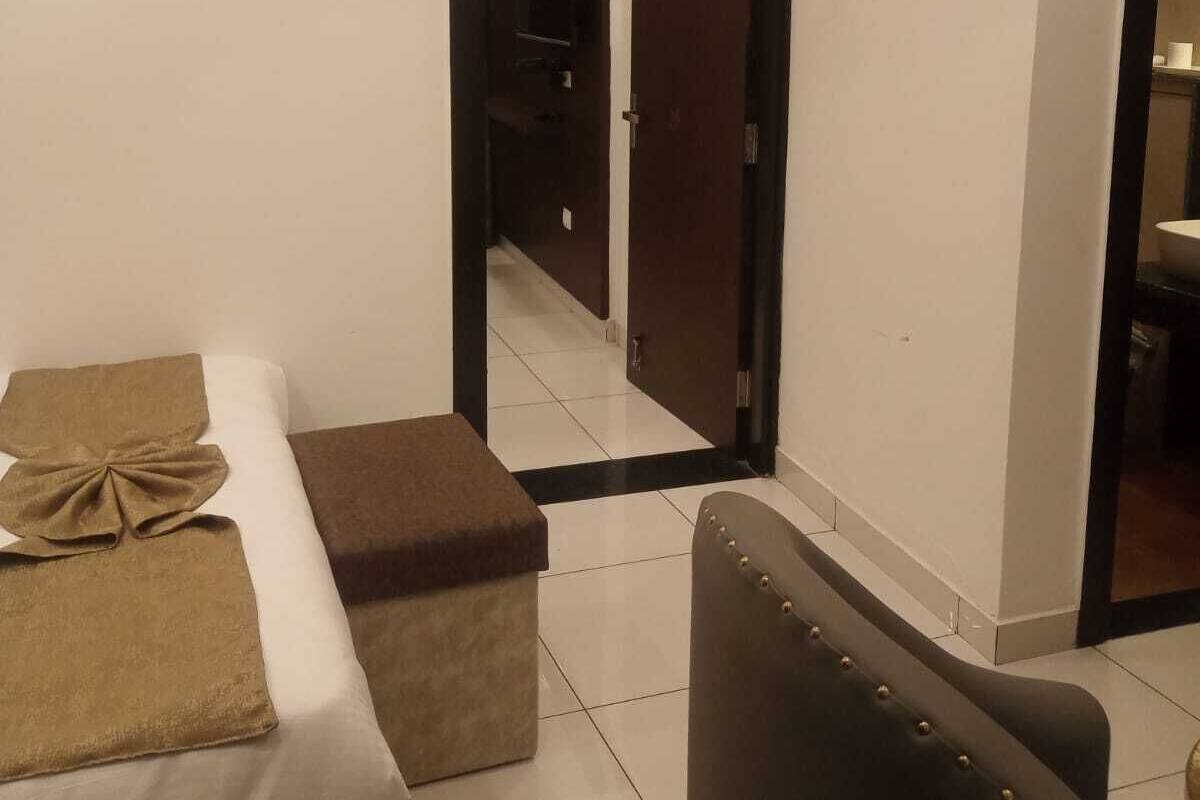 A hotel room with a bed, a seating area, a TV mounted on the wall, and a mirror.