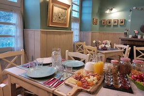 A breakfast setting with a wooden table, plates, cutlery, and a variety of food items including fruits, cheeses, and meats. - Old School Hotel (North Tzoumerka)