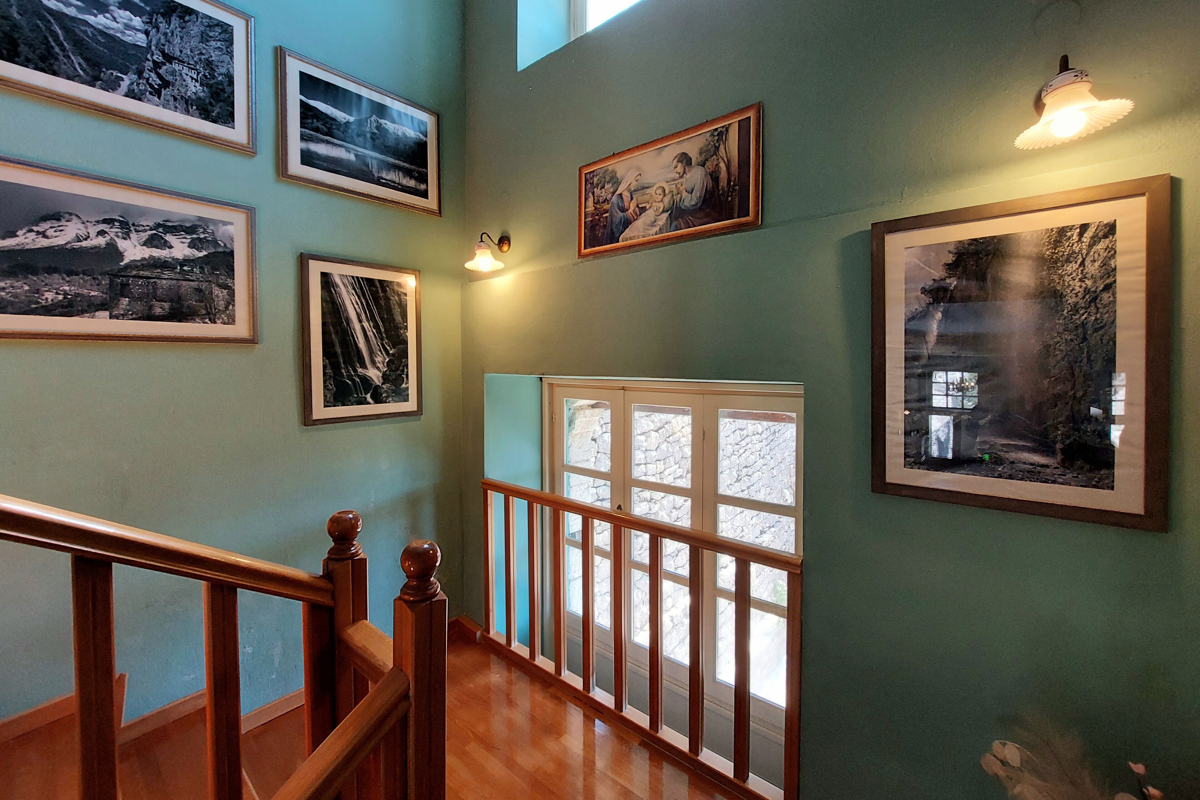 A hallway with wooden railings, framed photographs on the walls, and a large window with a view of the outdoors.