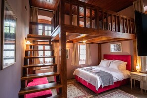 A bedroom with a red bed, a wooden ladder, and a window with curtains. - Old School Hotel (North Tzoumerka)