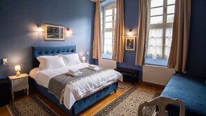Ein Schlafzimmer mit einem großen Bett, zwei Nachttischen, einem Beistelltisch, einer Bank und einem Fenster mit Vorhängen.