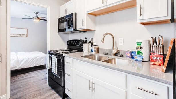 A compact kitchen with white cabinets, a stove, microwave, and a sink. - Cozy, Central 1B Apt Close to UC Hospitals, DT (Norwood)
