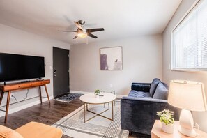 A modern living room with a flat-screen TV, a ceiling fan, a sofa, a coffee table, and a lamp. - Cozy, Central 1B Apt Close to UC Hospitals, DT (Norwood)