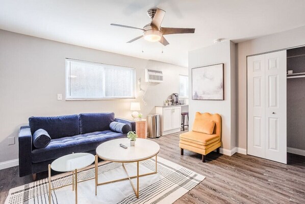 A living room with a blue sofa, an orange chair, a coffee table, and a ceiling fan.
