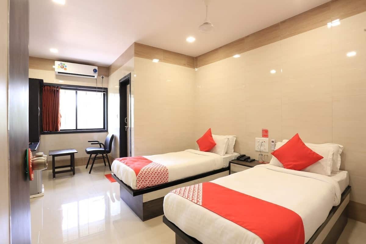 A hotel room with two beds, a desk, a chair, and a window.