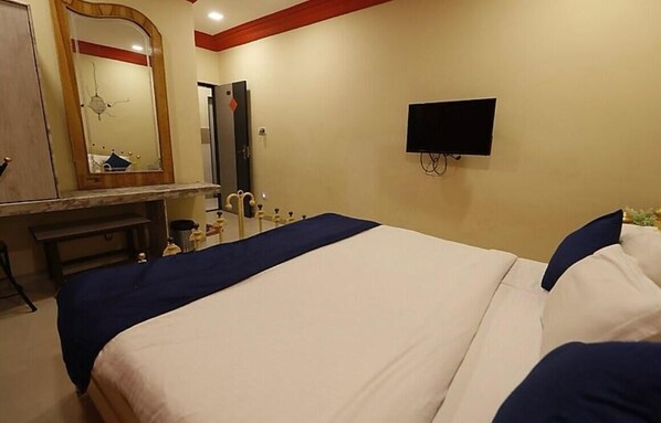 A hotel room with a bed, a TV mounted on the wall, a mirror, and a bench. - Hotel Suraj inn (Surat)