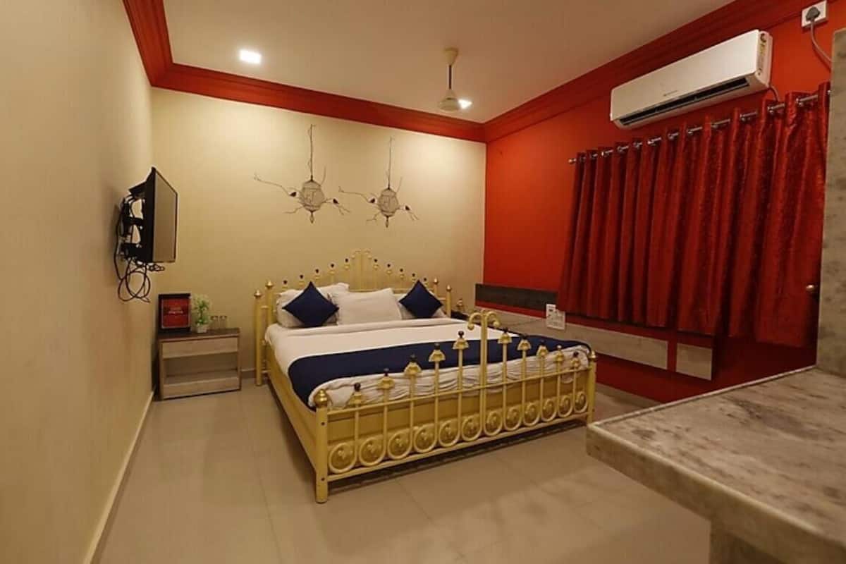 A bedroom with a bed, bedside table, nightstand, wall-mounted TV, air conditioning unit, and a red curtain.