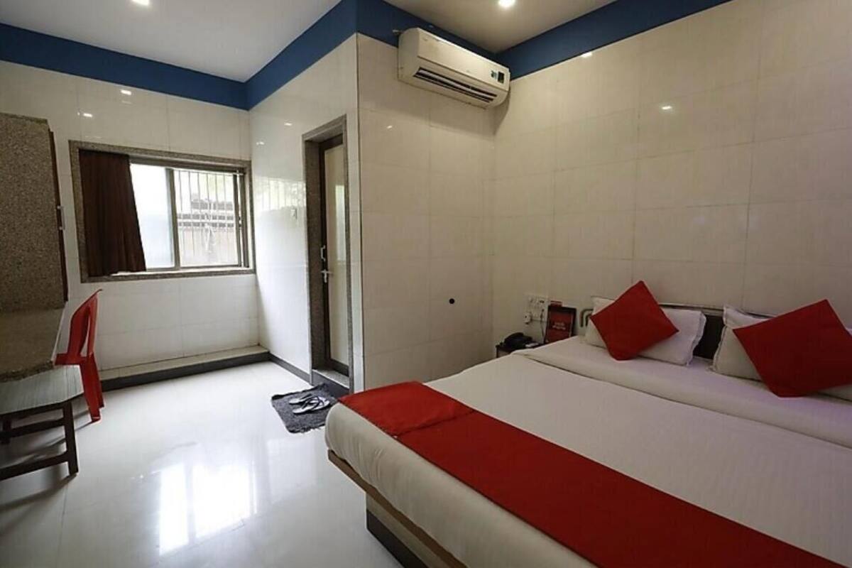 A hotel room with a bed, a window, an air conditioner, and a red chair.