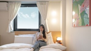 Ein Hotelzimmer mit Bett, einem Fenster mit Vorhängen, einer Nachttischlampe und einer Wand-Klimaanlage.