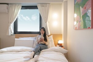 Habitación de hotel con cama, ventana con cortinas, lámpara de noche y aire acondicionado instalado en la pared.